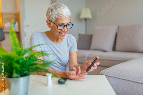 Happy mature woman with glucometer checking blood sugar level at home. Woman testing for high blood sugar. Woman holding device for measuring blood sugar photo