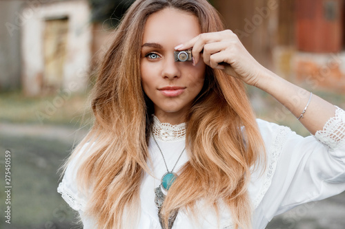 close-up portrait of a beautiful girl in a white dress holding a small retro camera near the eye