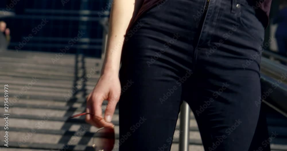 Slender girl on a city background close-up. She's wearing black slinky pants and a t-shirt tucked into her pants. The girl wears sunglasses and posing. Slender girl on a city background close-up. She's wearing black slinky pants and a t-shirt tucked into her pants. The girl wears sunglasses and posing.