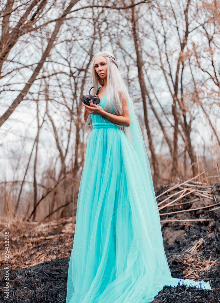 The girl in the forest is in a blue dress in the hands of holding a little dragon