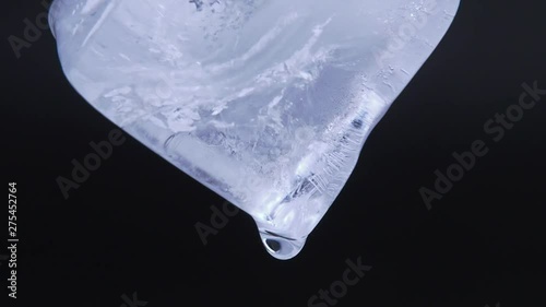 Macro video shooting of melting ice cube on black background. Real time process. Shot extra close up. Ice cube with falling down water drops