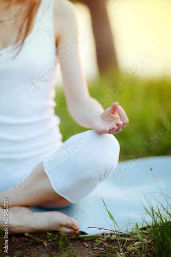 Woman doing meditation yoga mudra hands  on  knees and relax at blooming  lush meadow with green grass on the sunset or sunrise background. close-up