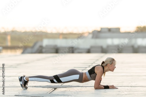 Attractive blonde girl in a sports suit doing yoga in the open air. Healthy lifestyle