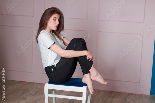 Girl in the studio on a pink background sitting on a chair