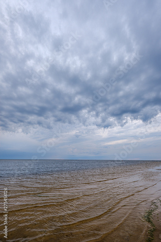 dramatic colorful clouds over sandy beach at the sea with blue sky