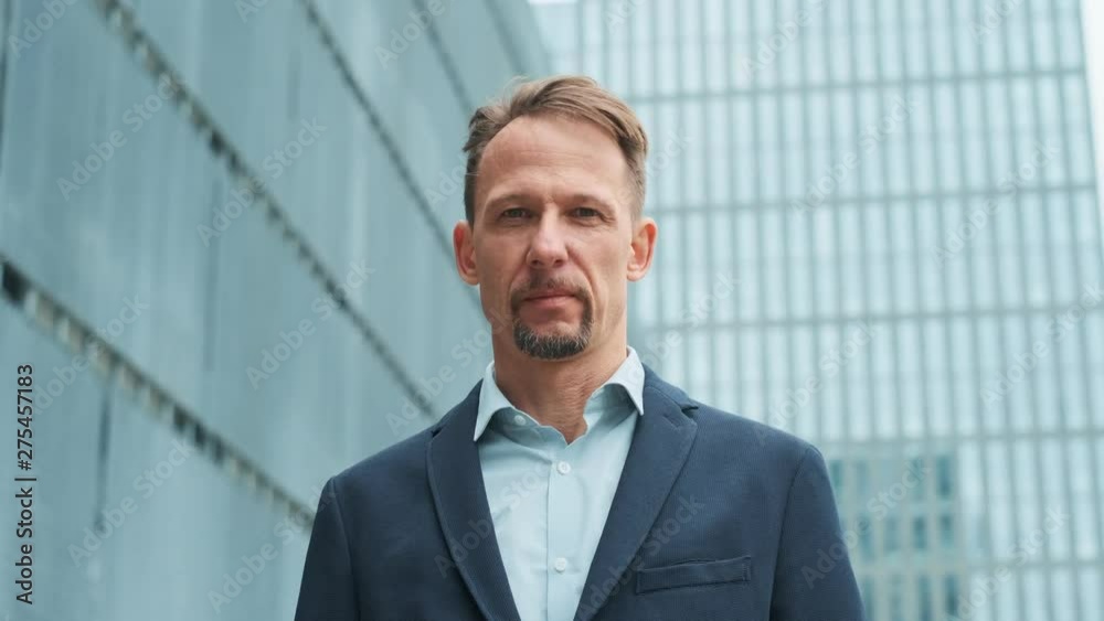 Portrait of a handsome businessman standing on a modern office building background and smiling broadly at the camera. A man proud and sure of himself, skyscraper background. Business, finance, banking