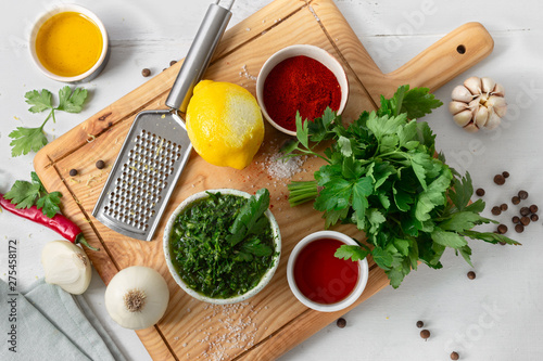 Top view cooking background. Raw ingredients for cooking green Chimichurri or Chimmichurri salsa or sauce on white wooden table