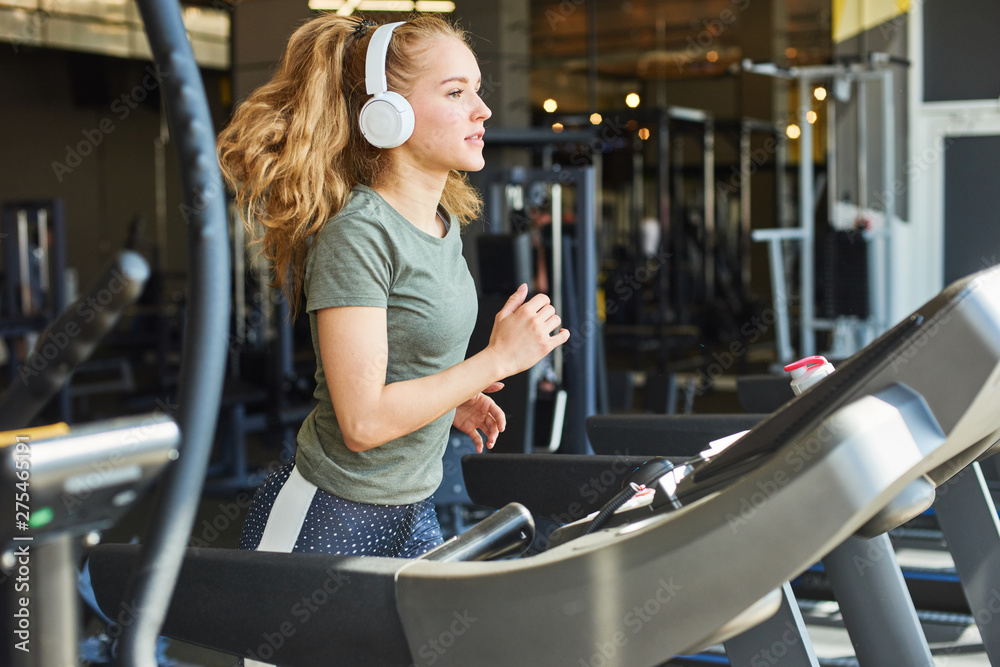 Fototapeta premium Girl in headphones running on the treadmill.