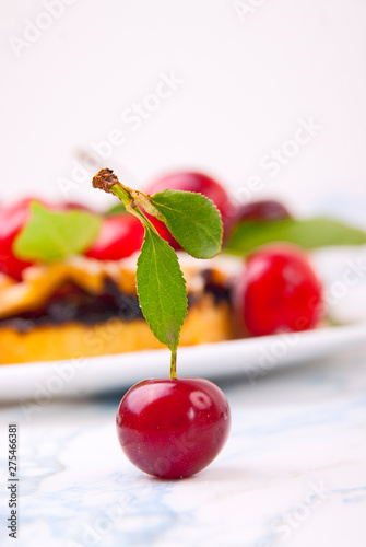 Cherry pie in the shape of a heart with fresh red cherries on the white marble table.