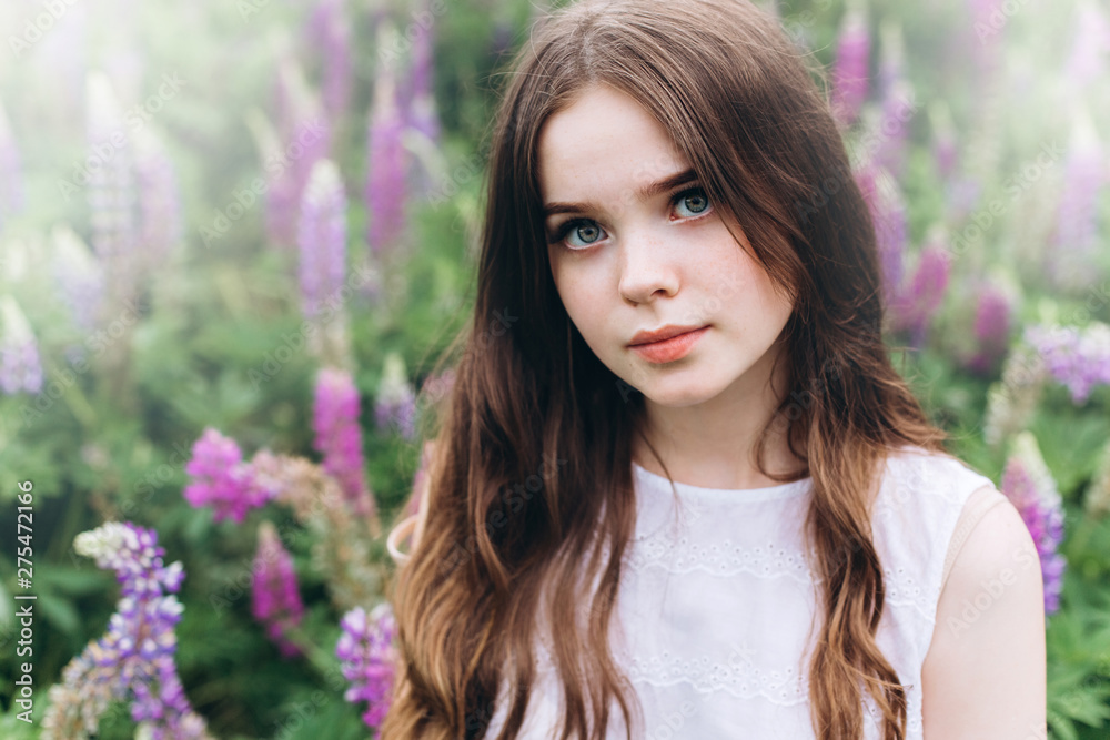 Portrait of young cute brunette girl in lupine violet field in blossom in summer sunset. Greenhouse, nature, natural beauty, freedom, youth concept Portrait of young cute brunette girl in lupine violet field in blossom in summer sunset. Greenhouse, nature, natural beauty, freedom, youth concept