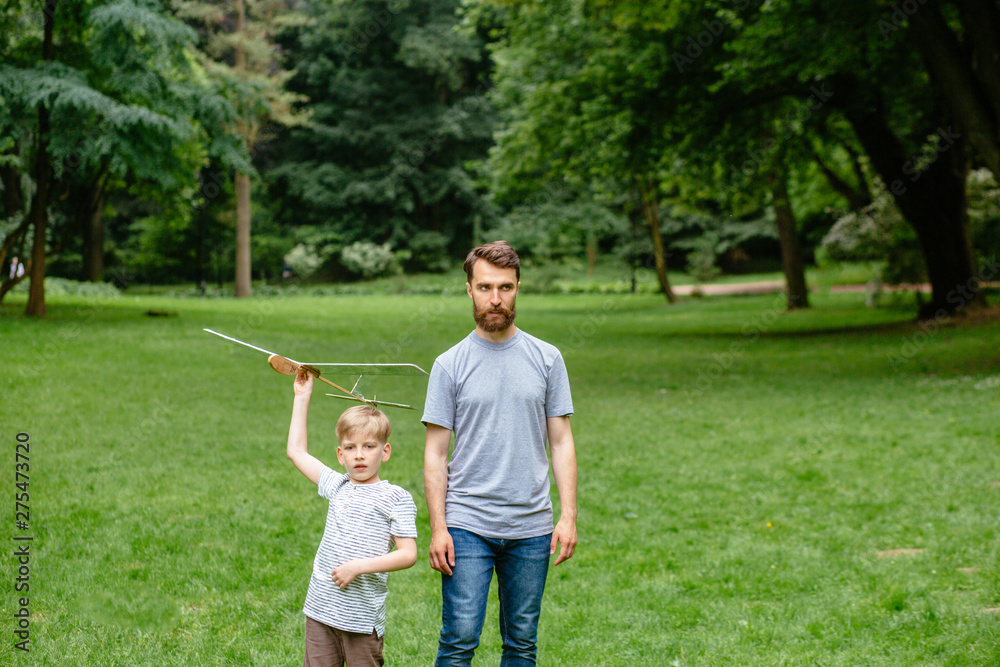 Obraz premium Dad and son together launch model airplane outdoors, both man and boy are looking cheerfully at plane. Father and son spending good time together, family relationships concept. Full leight