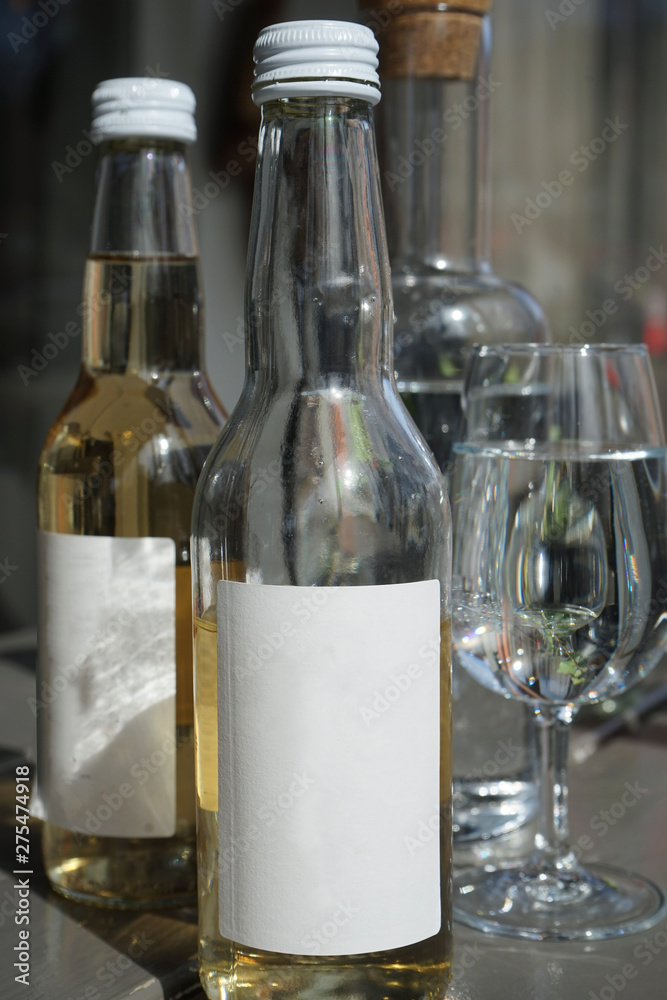 Side of a bottle with a white label. One half full and the other one full. with water glasses in the background. Side of a bottle with a white label. One half full and the other one full. with water glasses in the background.