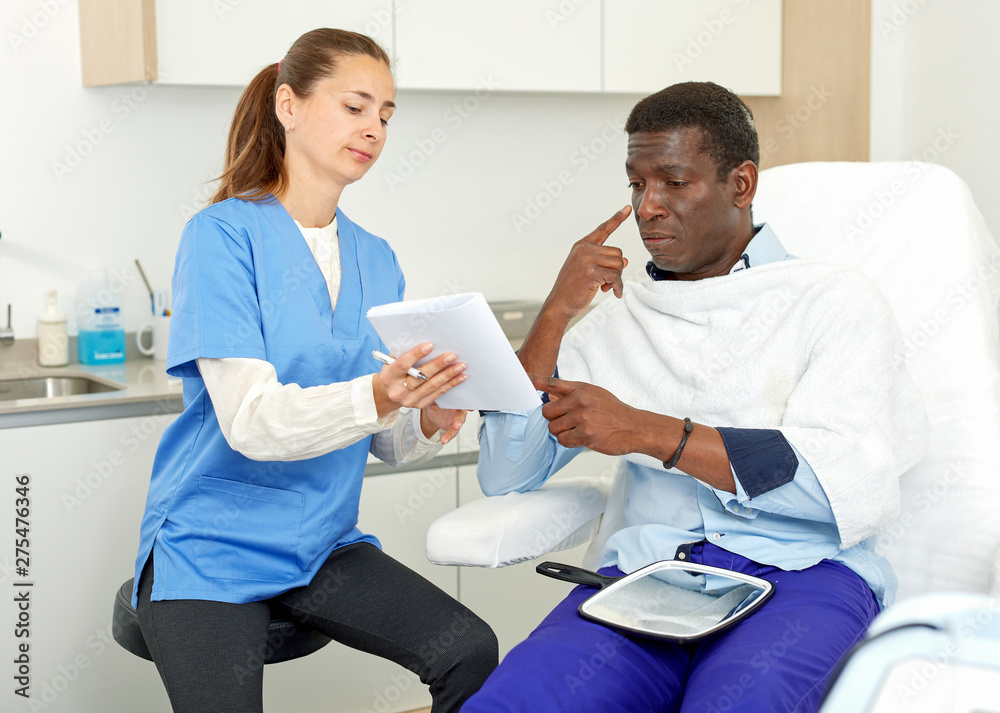 Obraz premium Cosmetician with papers talking to man before procedure in medical esthetic office