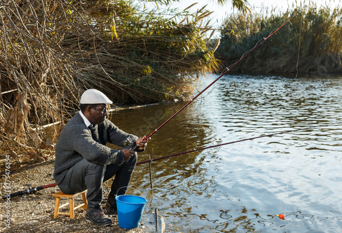 Positive fisherman sitting near river