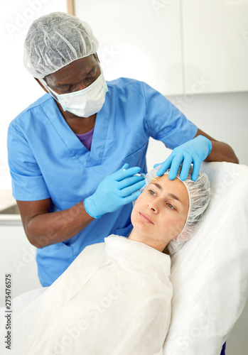 Doctor in mask is doing injection to woman patient in skin of face in estetic clinic