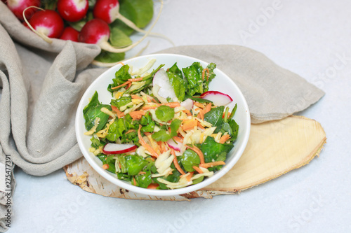 Fresh vegetable salad with greens and radishes, carrots and spinach leaves. Beautiful salad serving on the table, on a wooden stand in rustic style. Сoncept of healthy food, organic food, vegetarian