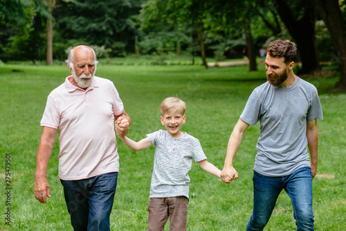 Portrait og happy family - grandpa, father and his son smiling walking together outdoor in park on background. Three different generation concept. © Iryna
