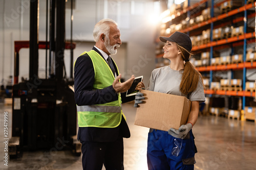 Happy mature manager talking to female distribution warehouse worker in industrial building. © Drazen