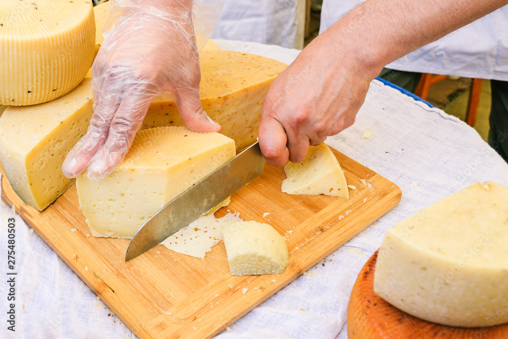 Man cuts fresh cheese. A wooden board and a white tablecloth on which lie the heads of the cheese. Closeup of slicing cheese. Different types of cheese. Man cuts fresh cheese. A wooden board and a white tablecloth on which lie the heads of the cheese. Closeup of slicing cheese. Different types of cheese.