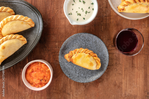 Empanadas with sauces and wine, shot from above on a dark rustic wooden background with a place for text