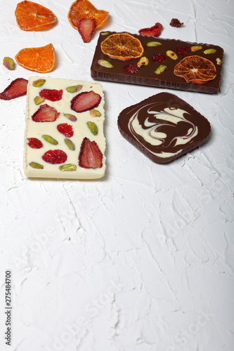 Homemade white and black chocolate. Decorated with slices of dried orange, strawberries, cherries and pistachios. On the surface covered with decorative plaster white.