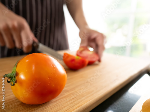 Professional chef man with stripe apron slicing red tomatoes by sharpen knife on wooden chopping board in the kitchen
