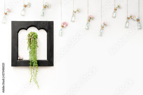 Ivy in black wooden frame on white wall with flowers in hanging bottles.