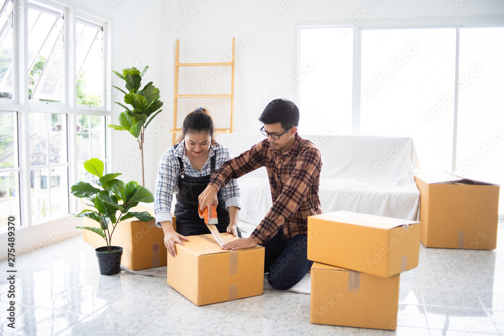 Asian couple family husband and wife packing box moving in new house or unbox for shopping online business living room with white color and sofa Asian couple family husband and wife packing box moving in new house or unbox for shopping online business living room with white color and sofa
