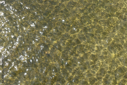 The sand is visible through the transparent texture of the water. River water and sandy bottom background. 