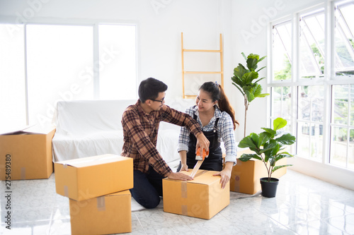 Asian couple family husband and wife packing box moving in new house or unbox for shopping online business living room with white color and sofa
