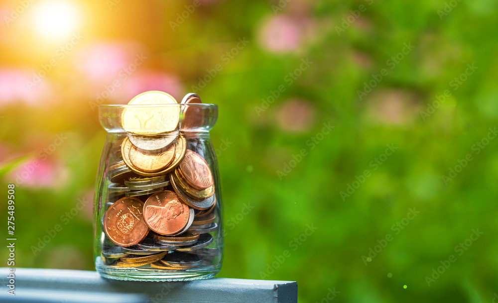 Conceptual image of saving money. Bottle of coins with nature background