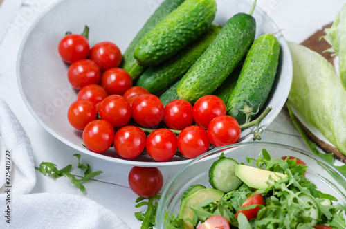 Fresh salad with cucumbers, cherry tomatoes, arugula, avocado, baby corn on white background. Vegetables on wood. Bio Healthy food, herbs and spices. Organic vegetables on wood.