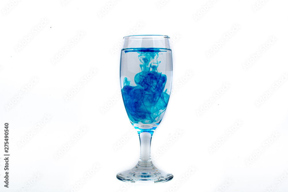 Blue food coloring diffuse in water inside wine glass with empty copyspace area for slogan or advertising text message, over isolated white background. Blue food coloring diffuse in water inside wine glass with empty copyspace area for slogan or advertising text message, over isolated white background.