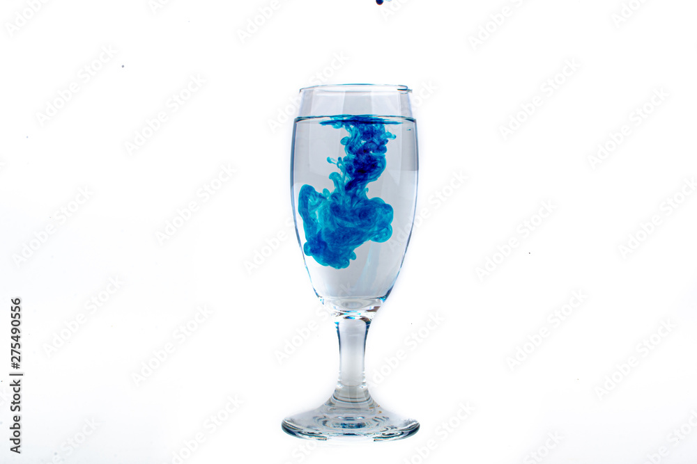 Blue food coloring diffuse in water inside wine glass with empty copyspace area for slogan or advertising text message, over isolated white background. Blue food coloring diffuse in water inside wine glass with empty copyspace area for slogan or advertising text message, over isolated white background.