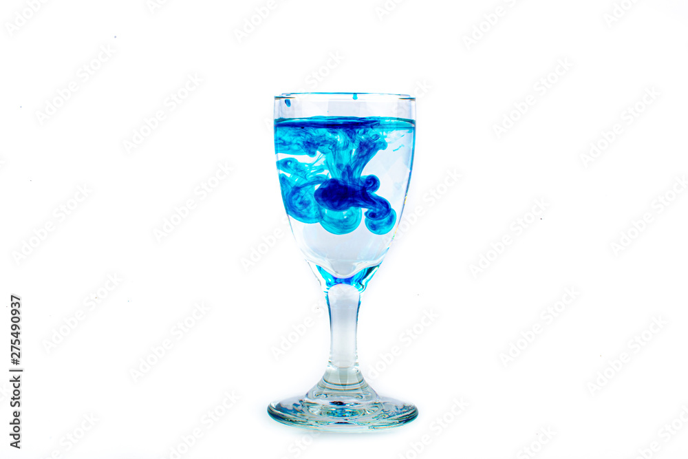 Blue food coloring diffuse in water inside wine glass with empty copyspace area for slogan or advertising text message, over isolated white background. Blue food coloring diffuse in water inside wine glass with empty copyspace area for slogan or advertising text message, over isolated white background.
