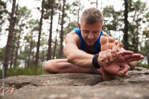 Man doing the head to knee pose in a forest