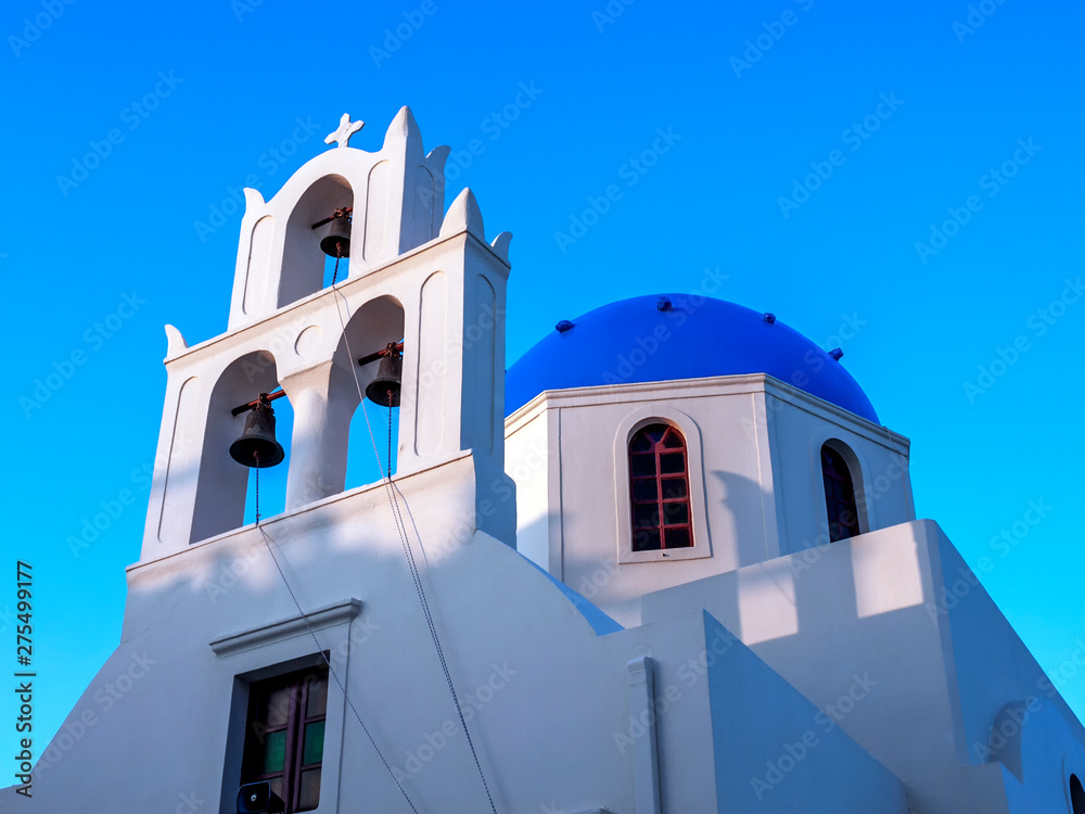 Greek Church with a clear blue sky showing three bells and a blue dome with windows and a bell rope at Oia on the island of Santorini. 