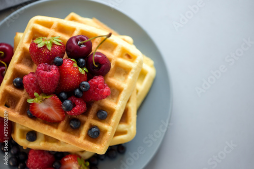 Top view on homemade belgian waffles with berries on gray table. Healthy breakfast concept.