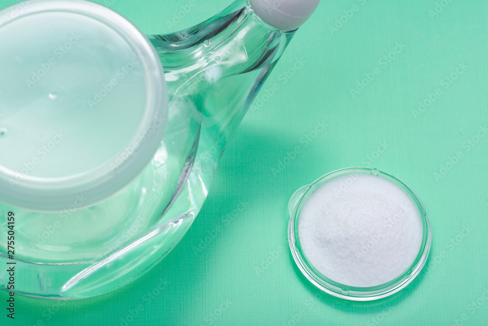 Neti Pot with Soft Comfort Tip and pile of saline (sodium bicarbonate and sodium chloride) on green background. Sinus wash. Nasal irrigation. Neti Pot with Soft Comfort Tip and pile of saline (sodium bicarbonate and sodium chloride) on green background. Sinus wash. Nasal irrigation.