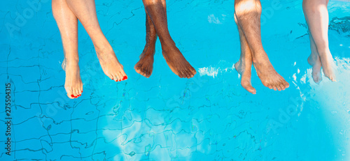 legs of four friends (common people) different race sitting by the swimming pool in sunny day. Party. Summer. Vacation and sport concept.