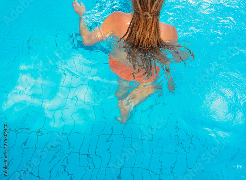 person's back (man or woman) with dreadlocks in the water in the swimming pool in sunny day. Vacation and sport concept.