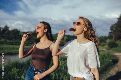 vacation and happiness concept, Two pretty sisters hipster girls having fun together, having ice cream, at sunset, in sunglasses,  positive facial expression, outdoor photo