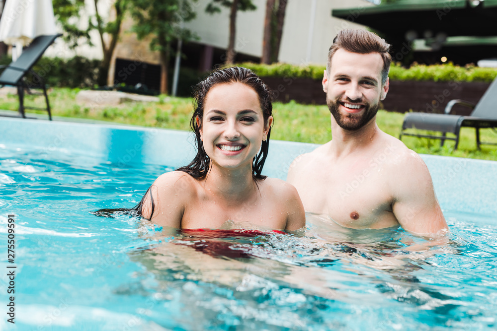selective focus of handsome bearded man smiling near attractive woman in swimming pool selective focus of handsome bearded man smiling near attractive woman in swimming pool