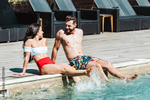 happy man looking at woman while sitting on wooden decks near swimming pool