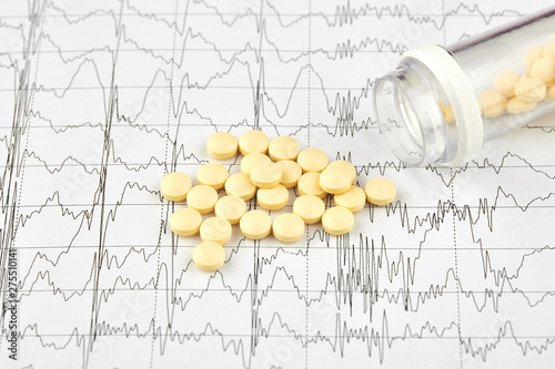 Close-up photo of yellow pills and vial on EKG graph