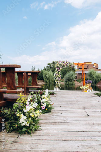 Stylish open space for a European wedding ceremony with wooden benches and a handmade arch. The arch is decorated with yellow flowers in the summer.