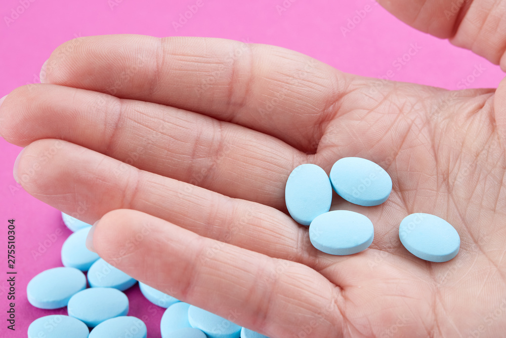 Close-up photo of blue pills in hand on pink background