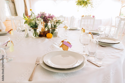 Table served for special occasion. Empty plate, glasses, forks, napkin and flowers on table covered with white tableclothes. Elegant dinner table. White table setting