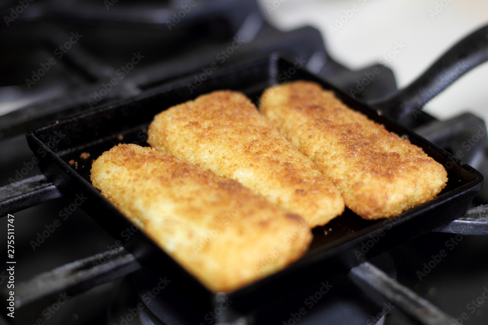 Fish sticks baked on a raclette pan resting on the stove top.