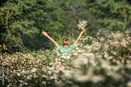 Handsome boy holding bouquet of fields camomile flowers in summer day. Back view.